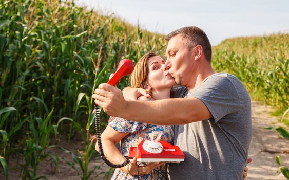 couple of kissing lovers take a comic selfie by retro phone in corn field on sunny summer day