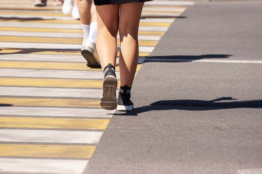 woman crossing the road at a crosswalk in the city on summer day. legs closeup