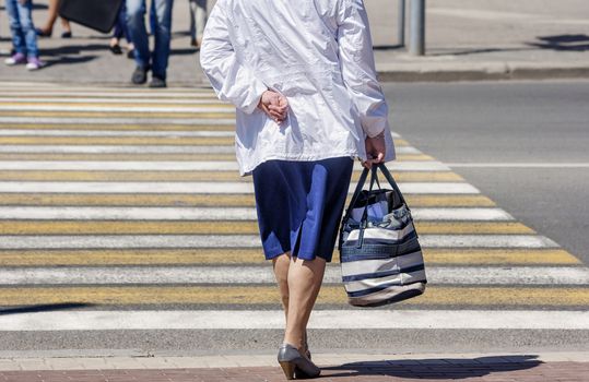 elderly woman is waiting to cross the road on sunny summer day