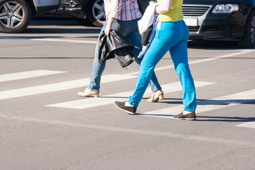 two women pedestrians walking on a crosswalk outside on sunny spring day