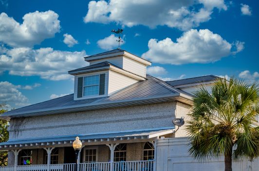 A white tabby building in the tropics with palm tree, cupola and weathervane