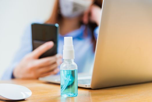 Asian young business woman wearing face mask protective using smart mobile phone for reading SMS message near laptop computer at home office quarantines disease coronavirus or COVID-19, work from home