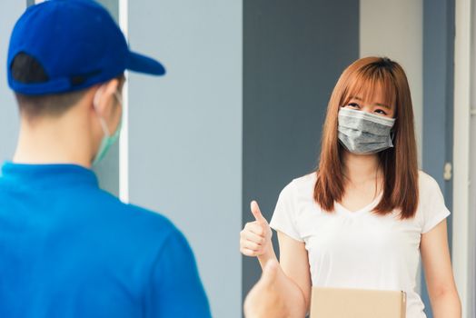 Asian delivery express courier young man giving parcel boxes to woman customer receiving both protective face mask and show thumbs up finger for good support sign, under curfew pandemic coronavirus