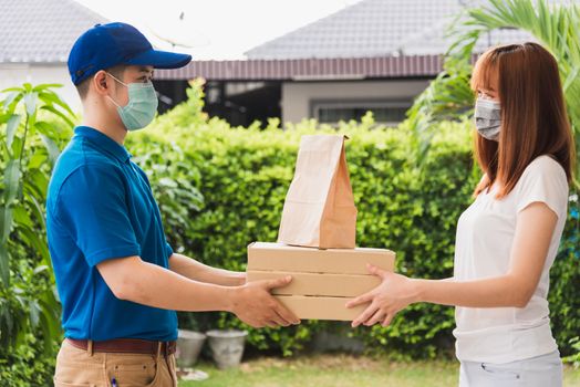 Asian delivery express courier young man giving paper bags fast food and pizza box to woman customer receiving both protective face mask, under curfew quarantine pandemic coronavirus COVID-19