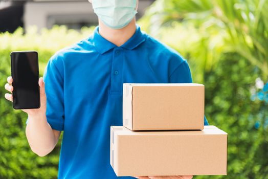 Asian delivery express courier young man giving boxes to customer he wears protective face mask at front home and show mobile phone blank screen, under curfew quarantine pandemic coronavirus COVID-19