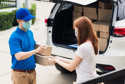 Asian delivery express courier young man use spray sterilize before giving boxes to woman customer receiving both protective face mask, under curfew quarantine pandemic coronavirus COVID-19