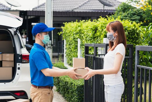 Asian young delivery man courier shopping online give package post box he protective face mask service woman customer receiving box at front home, under curfew quarantine pandemic coronavirus COVID-19