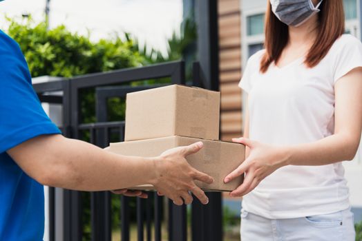 Asian young delivery man courier shopping online give package post box he protective face mask service woman customer receiving box at front home, under curfew quarantine pandemic coronavirus COVID-19