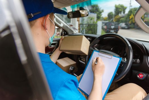 Asian delivery courier young man driver inside the van car with parcel post boxes checking amount he protective face mask, under curfew quarantine pandemic coronavirus COVID-19