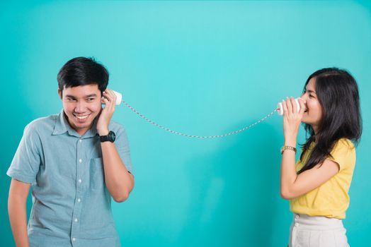 Asian happy young couple beautiful handsome smile and talking together with paper can telephone in a studio shot on blue background with copy space for text