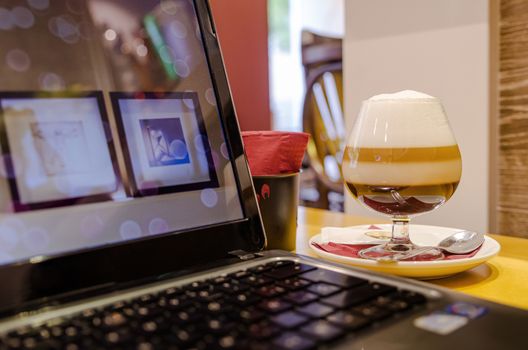 Laptop with wallpaper symbol & and some pictures, on a restaurant table to work while having an Irish coffee