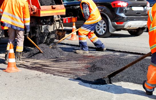 The group of road workers updates part of the road with fresh asphalt, using shovels, and levels it to repair the carriageway.