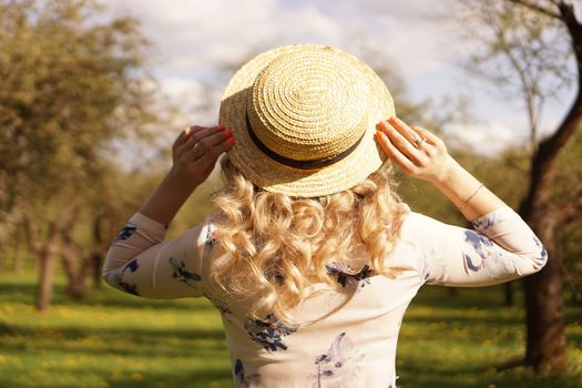 Girl in a straw hat in garden. Back view. Trendy casual summer or spring outfit