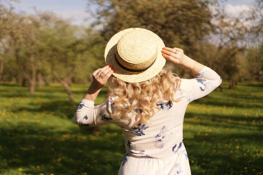 Girl in a straw hat in garden. Back view. Trendy casual summer or spring outfit