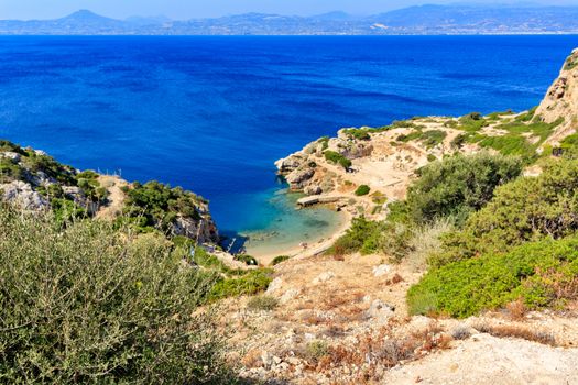 Rigid shrubbery grows on the rocky slopes of the Greek Corinthian Gulf on the background of a blue lagoon on the coast, a beautiful view from above, image with copy space.