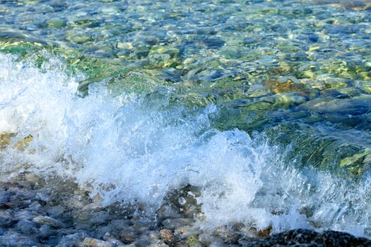 Beautiful sea wave with transparent and turquoise foam on a pebble beach, image with copy space.