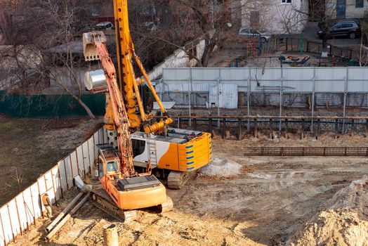 Heavy construction equipment, an excavator and a large powerful crane drill holes in the ground for laying concrete piles in the foundation of the future home, image with copy space.