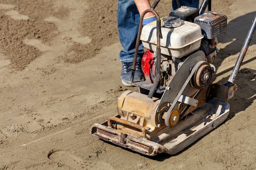 An old worn gasoline compactor needs to be cleaned and inspected for further work on compacting sandy soil, image with copy space.