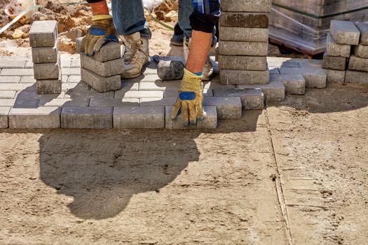 A worker lays paving slabs on a bright sunny day on a prepared smooth sand base on the pavement, image with copy space..