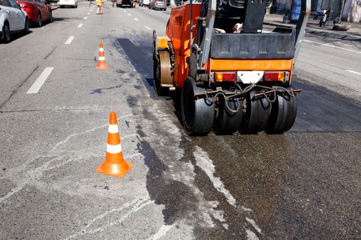 Heavy orange vibrating roller compacts hot asphalt renews a part of the road of the city street, image with copy space.