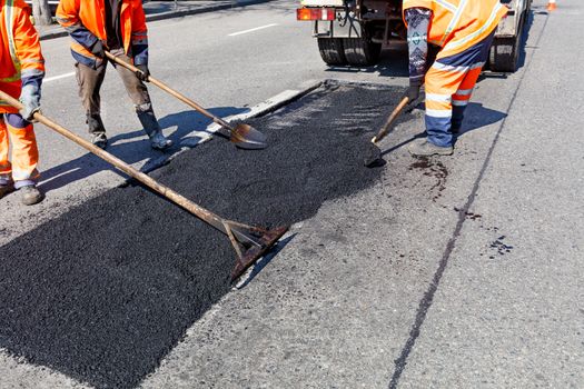 A working group of road workers accurately levels fresh asphalt on a part of the road for repair in road construction, image with copy space.