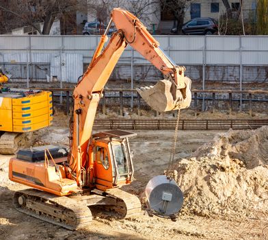 A heavy crawler construction excavator lifts and carries a large mortar mixer for laying concrete piles in the foundation of the future home, image with copy space.