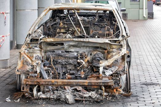 A burnt car is standing on the sidewalk of a city street, front view of a burnt out passenger compartment.