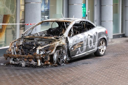 A burned-out car stands on the sidewalk of a city street, side view of a burned-out passenger compartment, image with copy space.