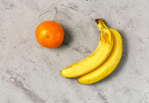 Yellow ripe bananas and orange mandarin on a gray concrete background, flat lay, image with copy space.