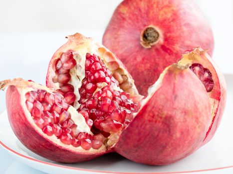 The Ripe pomegranate fruit and broken into four parts, on a white porcelain plate. The plate with a pomegranate border.