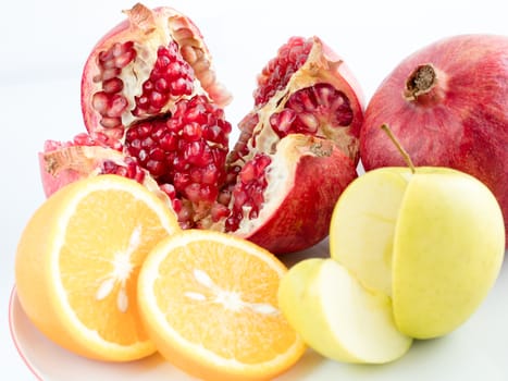 Ripe fruit: pomegranate, orange, apple, sliced on a white background. A ring of orange, an apple slice and a piece of pomegranate.
