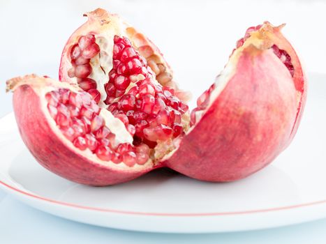 The Ripe pomegranate fruit and broken into four parts, on a white porcelain plate. The plate with a pomegranate border.