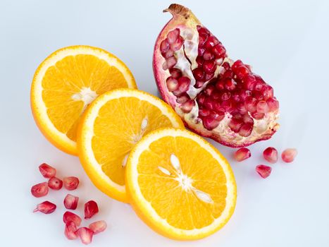 Three rings of sliced juicy ripe orange and a piece of pomegranate with individual grains on a light blue background