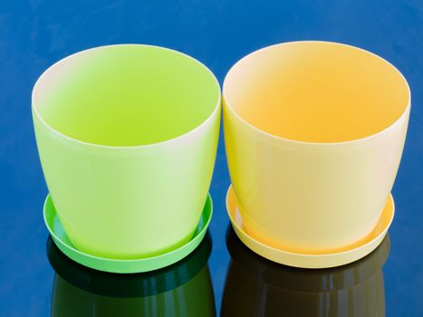 Green and yellow empty flowerpot on a glossy blue surface stand side by side on plates
