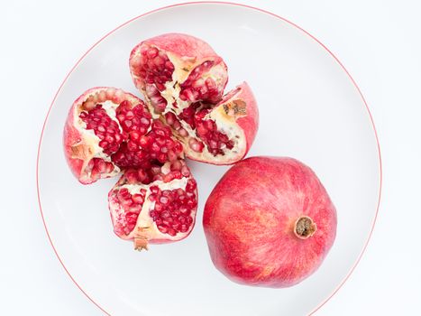 Two ripe pomegranate fruit and broken into four parts, on a white porcelain plate. The plate with a pomegranate border.
