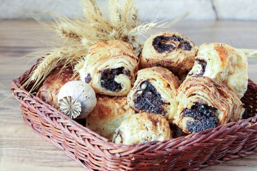 Sweet buns with poppy seeds lie in a wicker basket, on a wooden table and near a stone wall - sandstone. Poppy head and spikelets lie on sweet rolls