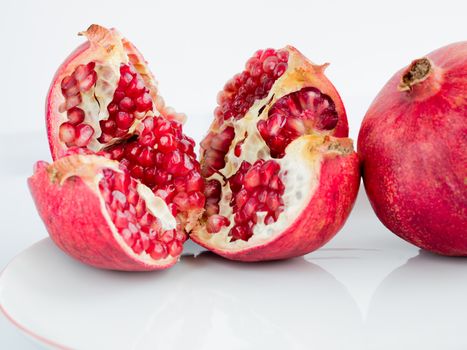 The Ripe pomegranate fruit and broken into four parts, on a wite porcelain plate. The whole garnet fruit is to the right of the cut.