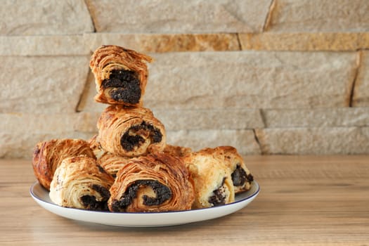 Sweet buns with poppy seeds on a white porcelain plate with a blue rim and on a wooden table and against a wall of stone - sandstone.