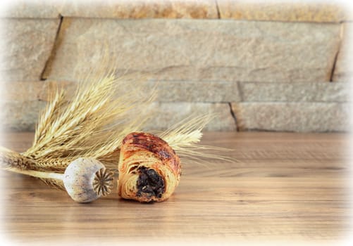 A sweet roll with poppy lies on a wooden table and near a stone wall - sandstone. Poppy head and spikelets lie near sweet roll