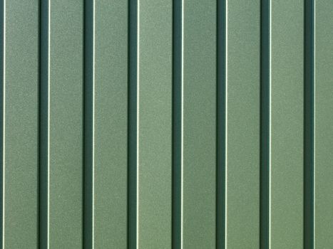 Greenery metallic fence made of corrugated steel sheet with vertical guides. Corrugated green iron sheet background close up.