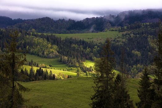 The sunlight makes its way through dense mountain clouds and illuminates the valley in the Carpathian mountains