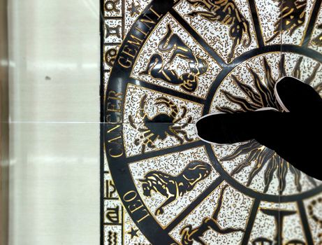 A cancer pointing at her zodiac sign, cancer on a circle of zodiac signs made on the floor in golden and black of a building