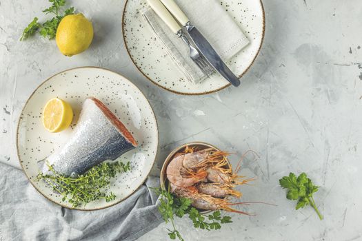 Trout fish  surrounded parsley, lemon, shrimp, prawn in ceramic plate. Light gray concrete table surface. Healthy seafood background.