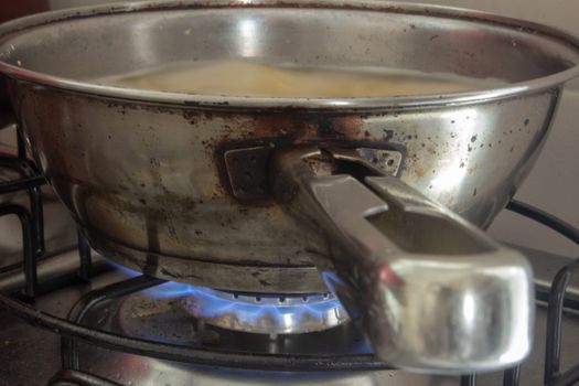 Iron pan boiling some water with pasta on a stove with the fire on