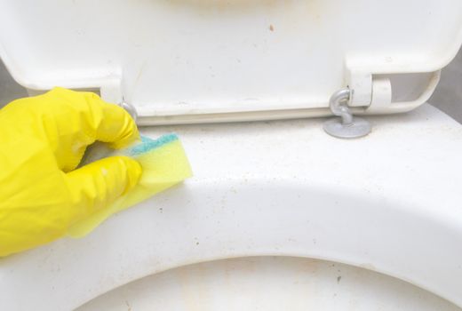A man in a yellow protective glove washes the dirty rim of the toilet with a sponge in bathroom.Regular domestic cleaning
