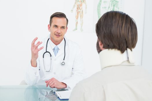 Friendly male doctor in communication with patient at desk in medical office