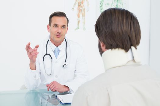 Friendly male doctor in communication with patient at desk in medical office