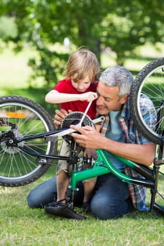 Happy father and his son fixing a bike on a sunny day