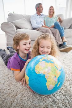 Happy children exploring globe while parents sitting on sofa at home