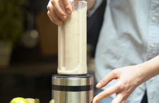 Close up female hands cooking almond milk. In a transparent blender glass, mix almonds with water. Healthy lifestyle and eating concept